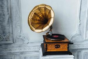 Old gramophone with horn speaker stands against anicent background, produces songs recorded on plate. Music and nostalgia concept. Gramophone with phonograph record photo