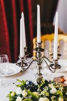 Luxurious banquet table served with beautiful candlestick with white candles, nice flowers, tablecloth and dishes. Retro style restaurant. Wonderful elements of decor. Table prepared for celebrating photo