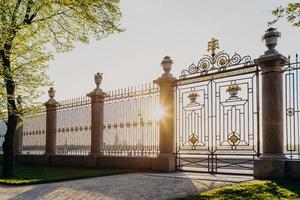 puertas del jardín de verano en rusia, san petersburgo. día soleado de primavera. hermosos árboles verdes y hierba. valla con puerta. obra maestra de la arquitectura foto