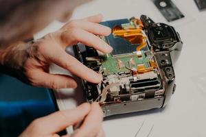 Technician engineer repairs broken photo camera with special tool. Photographer busy with maintenance. Selective focus. Technology repair