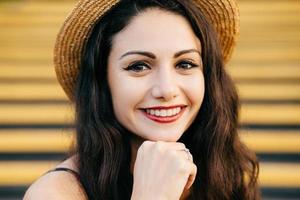 People, beauty, emotions concept. Close up portrait of beautiful brunette female with nice make-up and thin red lips smiling gently demonstrating her white teeth while keeping her hand under chin photo