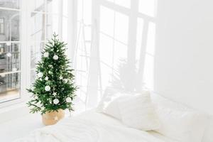 Decorated festive Christmas tree in white classic bedroom interior with soft bed. Winter home interior. Cozy season. New Year, celebration photo