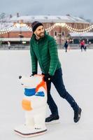 People, leisure, active lifestyle concept. Cheerful middle aged male learns to skate, uses skate aid, spends free time on skating rink, looks joyfully aside, enjoys spending weekends actively photo