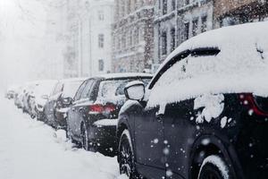 Snow covered city and cars. Heavy snowfall. Much snow. Cars parked on parking place during winter weather. Season and trasportation concept. Snowstorm