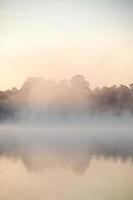 A mist drifts over the pond as the sun gradually lights the sky, the scene offering a moment of serenity and reflection. photo