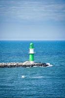 green white lighthouse on the Warnow River in Rostock. Waves on the stone edge photo