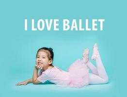 Beautiful smiling Asian little girl in a pink suit is dancing a ballet at school, empty space in studio shot isolated on colorful blue background photo