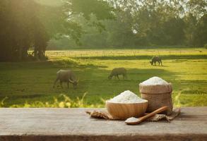 arroz jazmín en tazón y saco sobre mesa de madera con el fondo del campo de arroz foto