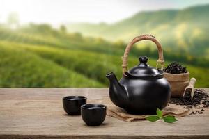 Cup of hot tea with teapot, green tea leaves and dried herbs on the wooden table in plantations background with empty space, Organic product from the nature for healthy with traditional photo