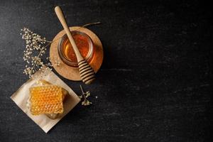 panal con cucharón de miel y flor seca sobre fondo negro, productos de abejas por concepto de ingredientes naturales orgánicos foto