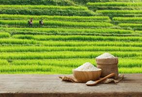 Jasmine Rice in bowl and burlap sack on wooden table with the rice field background photo