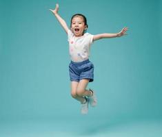 Playful energetic Asian little girl jumping in mid-air, empty space in studio shot isolated on colorful blue background photo