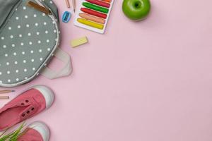 Creative flatlay of education pink table with backpack, student books, shoes, colorful crayon, empty space isolated on pink background, Concept of education and back to school photo