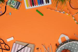 Top view mockup of Education's accessories with backpack, student books, camera toy, colorful crayon, eye glasses, empty space isolated on orange background, Concept of education and back to school photo