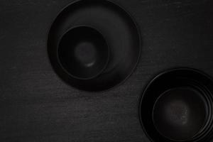 grupo de cuencos y platos redondos de cerámica negra en blanco vacíos en suelo negro de piedra negra, vista superior del concepto tradicional de utensilios de cocina hechos a mano foto