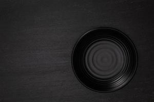 Empty blank black ceramic round bowl on black stone blackground with copy space, Top view of traditional handcrafted kitchenware concept photo