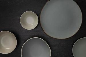 Group of empty blank ceramic round bowls and plates on black stone blackground, Top view of traditional handcrafted kitchenware concept
