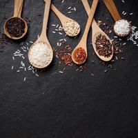White rice, Jasmine rice, Black rice, Brown rice, Riceberry and Mixed rice in wooden spoon over black table background with copy space for your