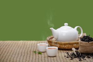 taza de té caliente con tetera, hojas de té verde y hierbas secas en la alfombra de bambú por la mañana aísle el fondo verde con espacio vacío, producto orgánico de la naturaleza para la salud con el tradicional foto