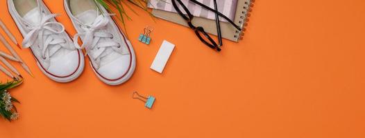 flatlay creativo de la mesa naranja de educación con libros de estudiantes, zapatos, lápiz de colores, anteojos, espacio vacío en una foto de estudio aislada en un fondo de pancarta largo naranja, concepto de educación