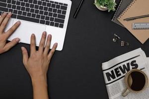 Top view workspace office supplies mockup with hands using notebook, hot coffee cup, glasses, books, newspaper and accessories on black table overhead view with copy space, Workspace for designer photo