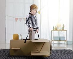 niña asiática jugando con artesanía de avión de juguete de cartón en la sala de estar con espacio de copia para su texto, creativa en casa y sueños de concepto de vuelo foto