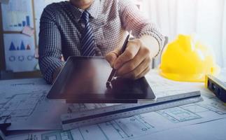 Two colleagues discussing data working and tablet, laptop with on on architectural project at construction site at desk in office photo