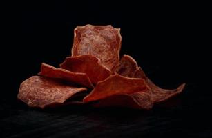 chips de carne sobre un fondo negro. hermoso placer de finas lonchas de carne seca. foto