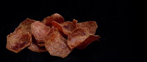 Meat chips on a black background. Beautiful placer of thin slices of dried meat. photo