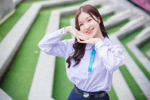 Beautiful high school Asian student girl in the school uniform stands and smiles happily with braces on her teeth while she arm crossing confidently with the building as a background. photo