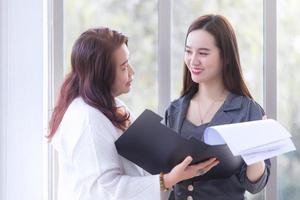 Young Asian business woman stands and talk to senior manager to consult about work intently in office. photo