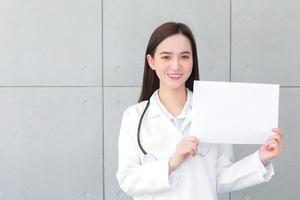 una doctora asiática que usa abrigo médico sostiene y muestra papel blanco para presentar algo en el concepto de atención médica. foto