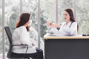 una doctora asiática que usa abrigo médico habla con una paciente para sugerir una guía de tratamiento y un concepto de atención médica en el consultorio del hospital. foto