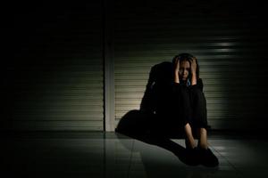 Woman depressed from sad stress pain despair problem, person sit on closed shop on corridor alone with emotion lonely desperate upset head down. Head in hand no way out concept, copy space photo