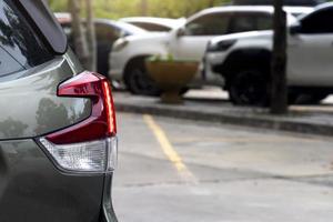 parte trasera del coche con luz trasera encendida en el estacionamiento. borrosos de varios autos estaban estacionados frente al estacionamiento bajo la sombra de los árboles. en camino de cemento. foto