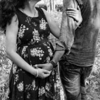 Indian couple posing for maternity baby shoot. The couple is posing in a lawn with green grass and the woman is falunting her baby bump in Lodhi Garden in New Delhi, India - Black and White photo