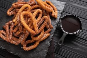 churros caseros con chocolate sobre un fondo rústico de madera oscura. foto