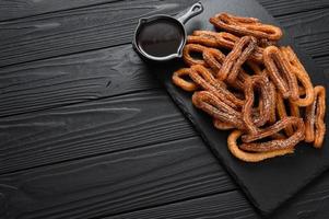 churros caseros con chocolate sobre un fondo rústico de madera oscura. foto