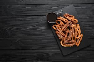 churros caseros con chocolate sobre un fondo rústico de madera oscura. foto