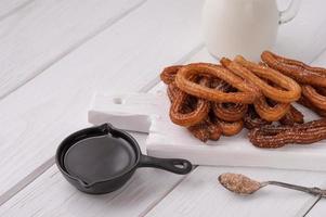 Homemade churros with chocolate on a white wooden background. photo