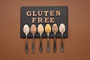 Gluten free text and spoons of various gluten free flour, almond, buckwheat, rice, corn, oat, chickpea. Flat lay, top photo