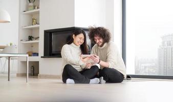 multiethnic couple using tablet computer in front of fireplace photo