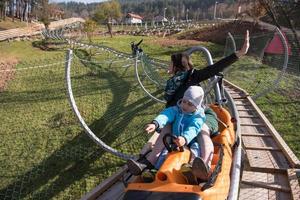 madre e hijo disfrutan conduciendo en una montaña rusa alpina foto