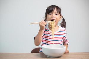 linda niña asiática comiendo deliciosos fideos instantáneos en casa. foto