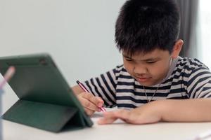 Kid self isolation using tablet for his homework,Child doing using digital tablet searching information on internet during covid 19 lock down,Home schooling,Social Distance,E-learning online education photo