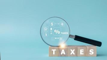 Magnifier glass with the icon of tax concept on the wooden cube. Business concept photo