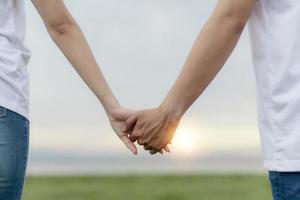 Couple hold hands in green field on sunset photo