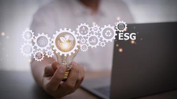 Businesswoman hand holding light bulb with esg icon on virtual screen, ESG Environmental, social and corporate governance concept. photo