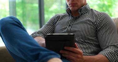 Man is Laying on Couch at Home and Using Tablet photo