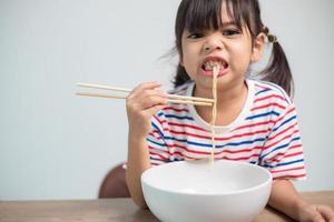 Cute Asian child girl eating delicious instant noodles at home. photo